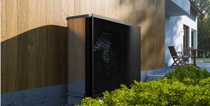 Schwarze Wärmepumpe an der Holzfassade eines Hauses mit Terrasse und Garten.
