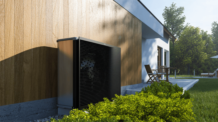 Schwarze Wärmepumpe an der Holzfassade eines modernen Hauses mit Garten und Terrasse.