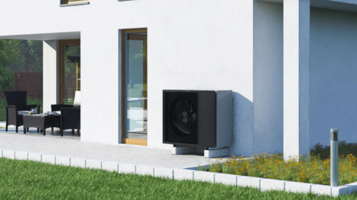 Dunkle Wärmepumpe an der weißen Fassade eines modernen Hauses mit Terrasse