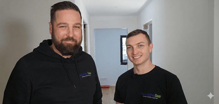 Zwei lächelnde Männer in HeizungsbauSaar-Kleidung in einem hellen Neubau